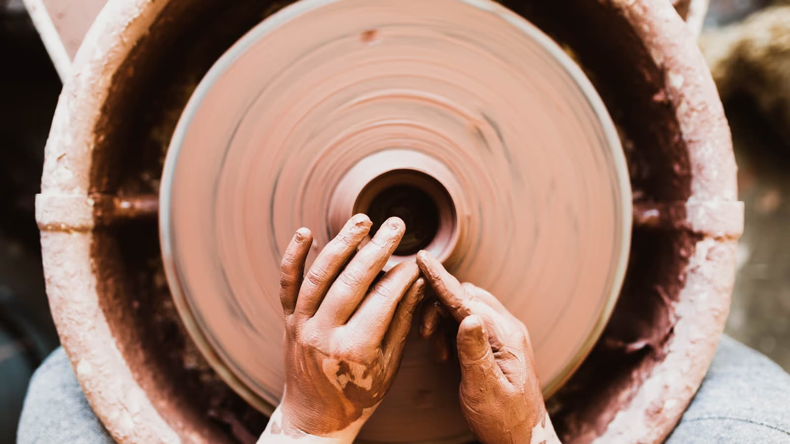 Mains d'un artisan potier façonnant un vase d'argile sur un tour en rotation, illustrant le quotidien du travail indépendant