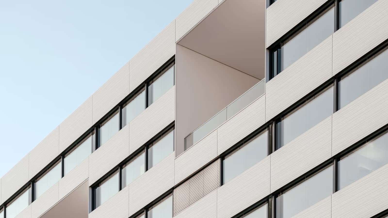 Façade claire d'un immeuble contemporain aux larges baies vitrées et balcons en retrait se détachant sur un ciel dégagé, évoquant l'investissement en pierre-papier