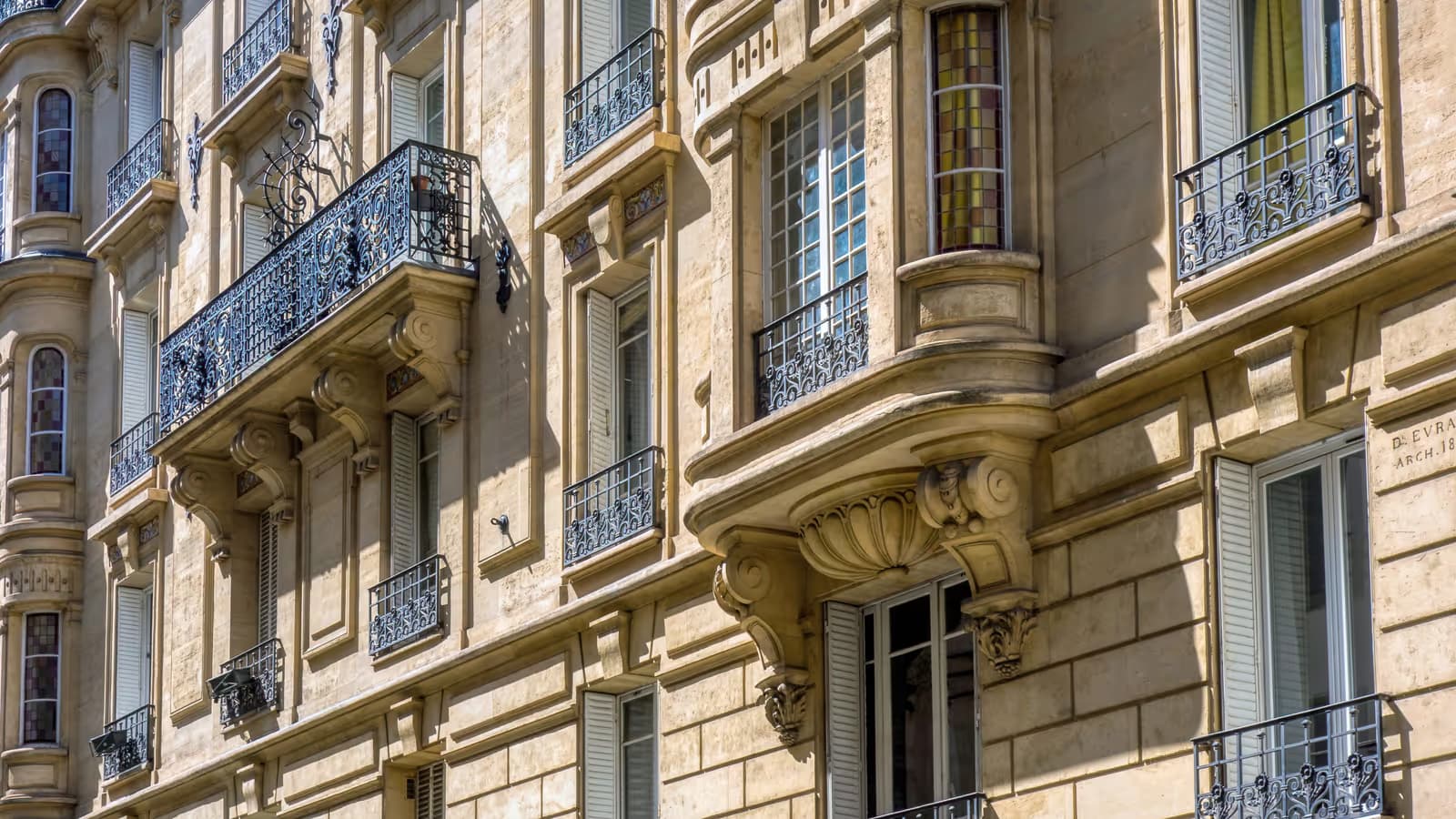 Façade d'un immeuble de rapport parisien en pierre de taille ensoleillée, avec balcons en fer forgé et rangées d'appartements urbains destinés à la location