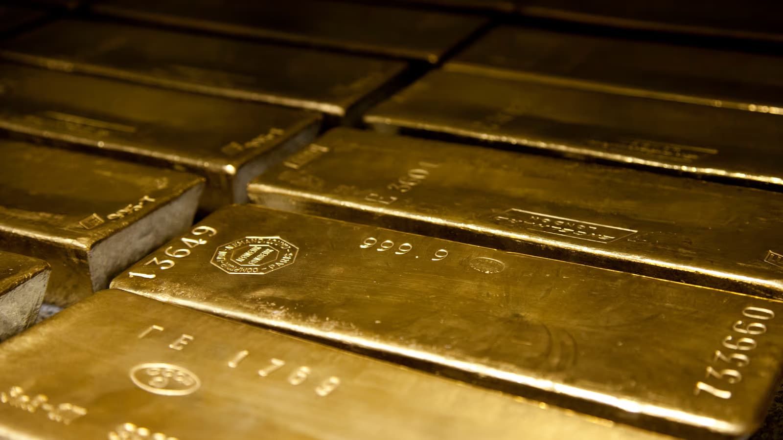 Rangées de lingots d'or standard rangés côte à côte dans une chambre forte, numéros de série et poinçons de fonderie gravés en surface sous une lumière chaude et tamisée