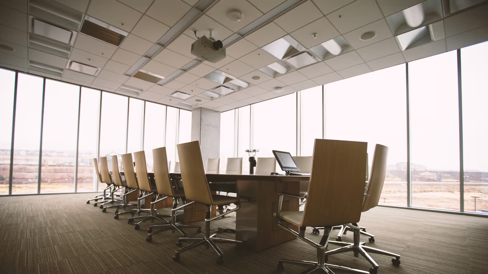 Salle de conseil d'entreprise inoccupée, longue table en bois bordée de fauteuils clairs, baies vitrées du sol au plafond baignées de lumière du jour