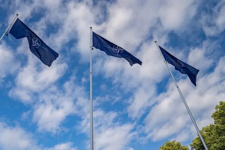Trois drapeaux de l'OTAN flottant dans un ciel bleu