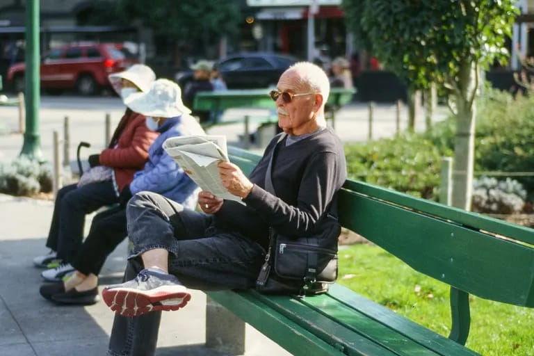 Homme assis sur un banc de parc lisant un journal