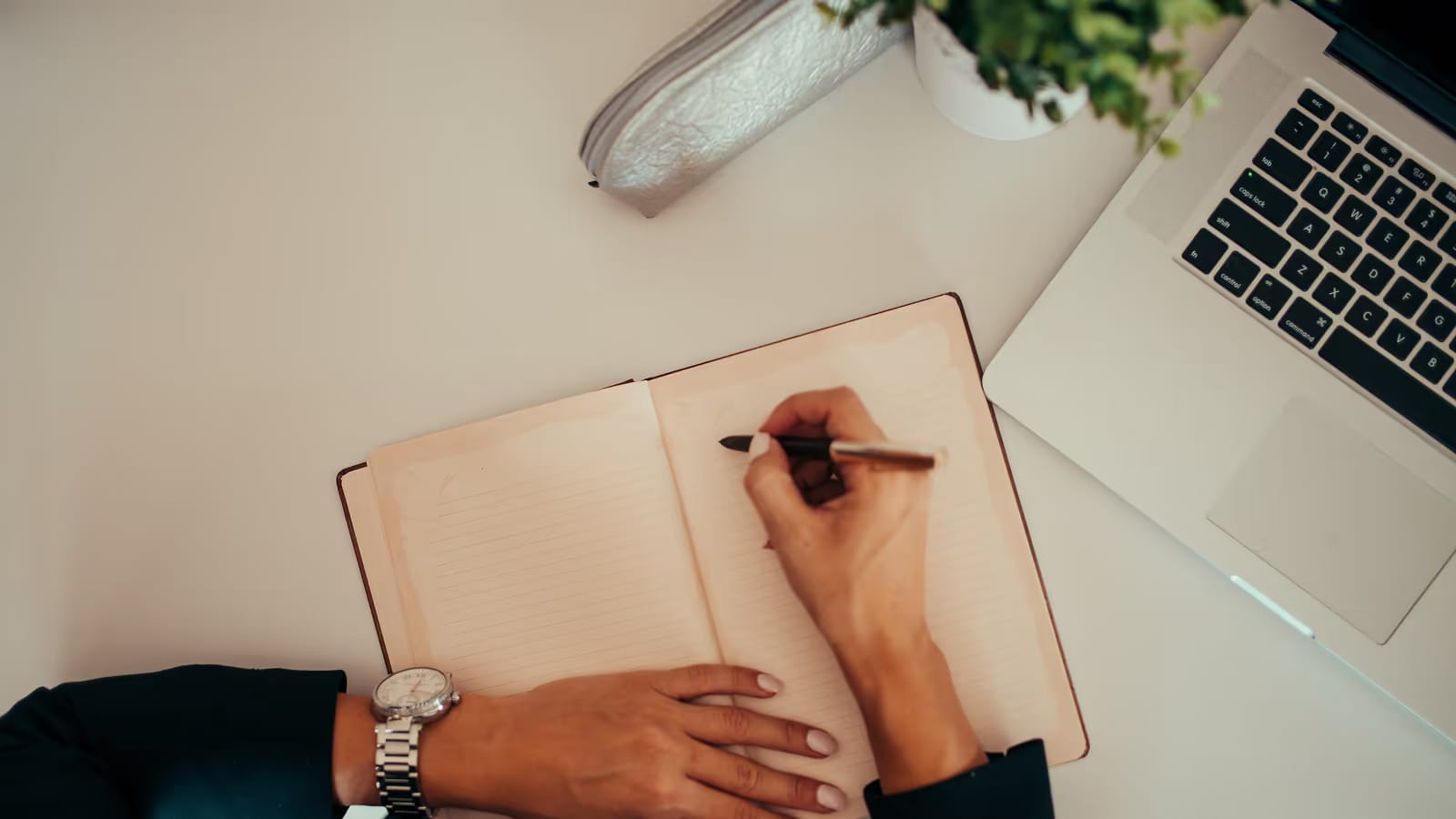 Personne écrivant dans un carnet devant un ordinateur portable sur un bureau épuré, comparaison d'offres