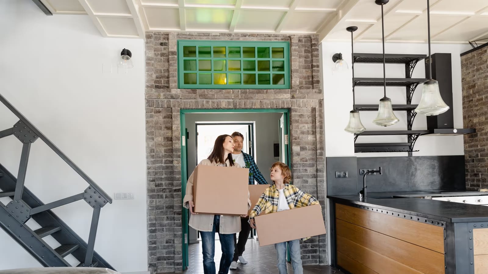 Une famille, parents et enfant, franchit le seuil de sa nouvelle maison en portant des cartons de déménagement, dans un intérieur chaleureux ouvert sur la cuisine