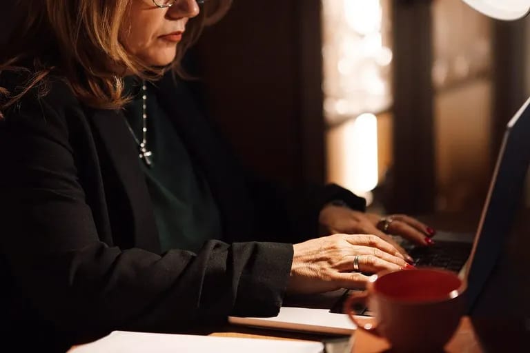 Femme en tailleur tapant sur un ordinateur portable près de documents et d'une tasse